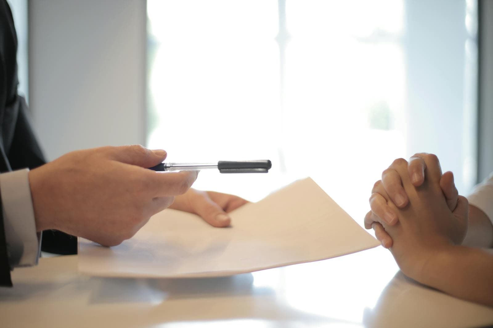 Close-up of a businessman handing a fountain pen across a contract on a desk, a stand-in for the $14 billion subordinated DeployCo deal OpenAI signed with nineteen private equity and consulting firms